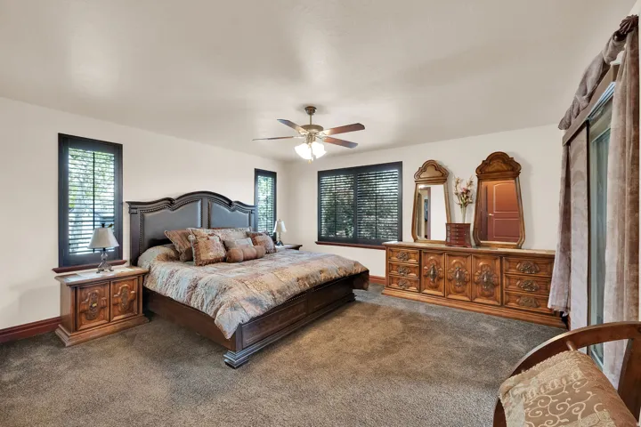 Carpeted room featuring a ceiling fan with integrated lighting, multiple windows with blinds, and a built-in sliding glass door