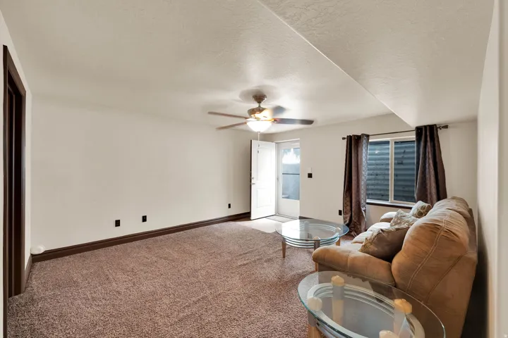Carpeted living area featuring white walls, dark wood-finish trim, and a ceiling fan with integrated lighting