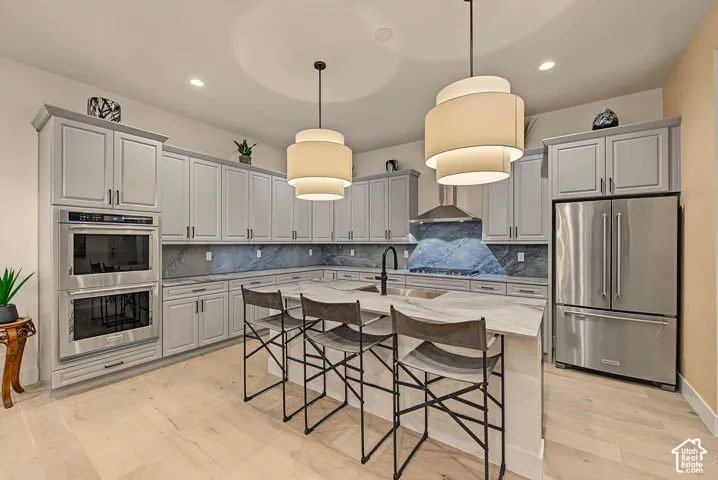 Light wood-finish flooring, light gray cabinetry, stainless steel appliances, large kitchen island with seating, and dual pendant lighting