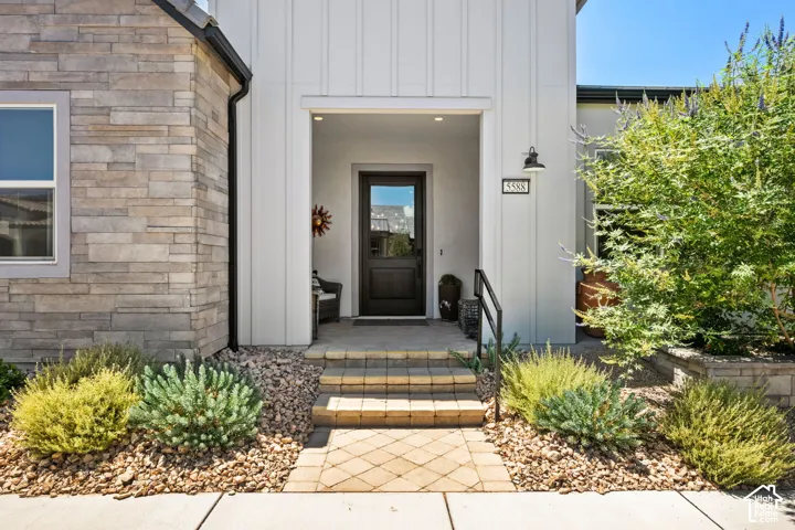 Contemporary exterior featuring a stone facade, board-and-batten siding, a covered entry with an inset door, paver walkway, and structured landscaping
