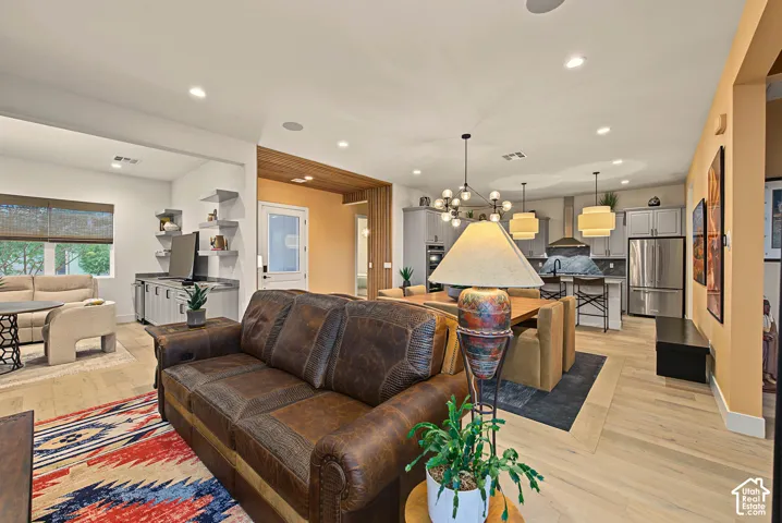 Open-concept living space with light wood-finish flooring, recessed lighting, and a kitchen featuring stainless steel appliances and pendant lighting