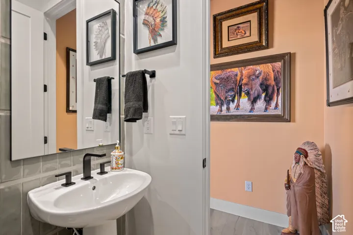 Pedestal sink with a matte black widespread faucet, framed wall mirror, gray subway tile backsplash, and light wood-finish flooring