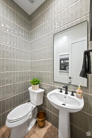Vertical tiled walls, pedestal sink, wall-mounted mirror, and wood-finish flooring