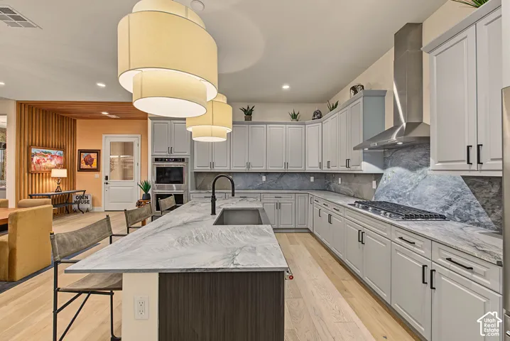 Spacious kitchen featuring an extended island with undermount sink, light wood-finish flooring, light-toned cabinetry, stainless steel appliances, and a unique backsplash