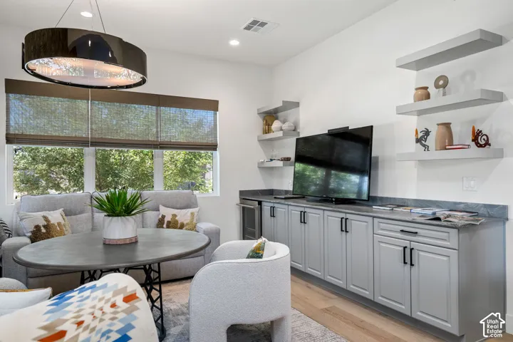 Recessed lighting illuminates the open living space featuring a built-in lower cabinetry unit with an integrated beverage refrigerator, floating wall shelves, and wood-finish flooring