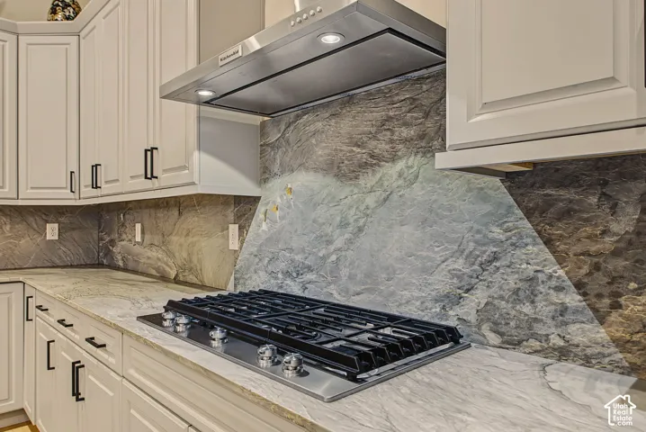 White shaker-style cabinetry with matte black hardware, stone countertops, and a gas cooktop with a stainless steel range hood