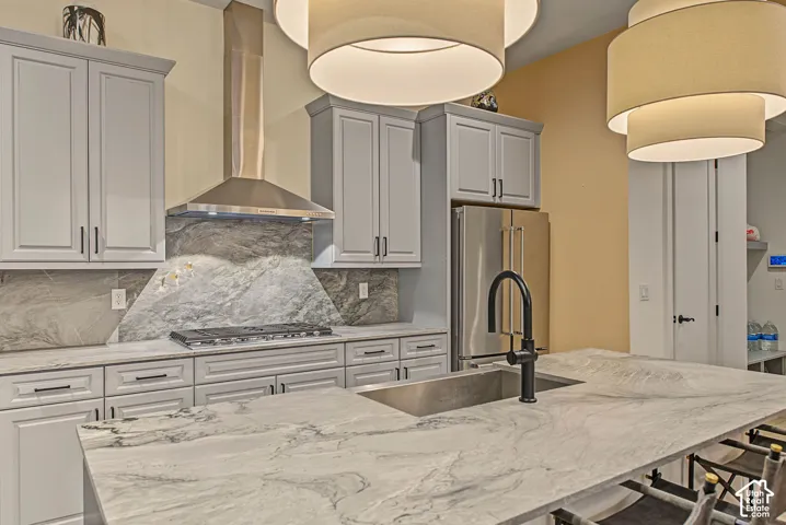 Kitchen featuring light gray cabinetry, stainless steel appliances, a gas range with a stainless steel vent hood, and natural stone countertops with matching backsplash