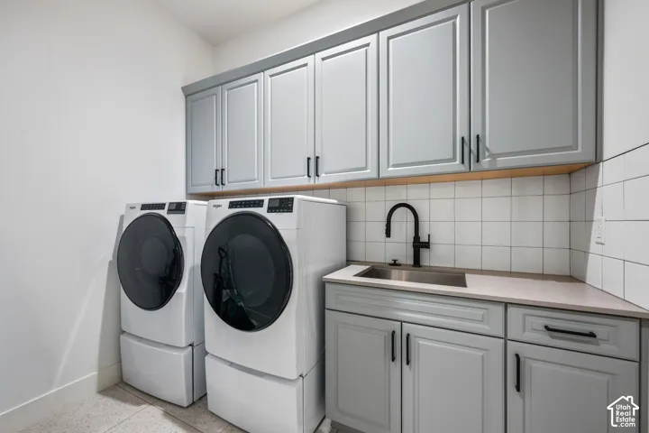 Laundry area featuring light gray cabinetry, a utility sink with a black gooseneck faucet, light-toned countertop, and white square tile backsplash