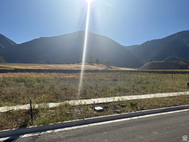 Expansive undeveloped lot featuring a paved road, concrete sidewalk, and mountain backdrop