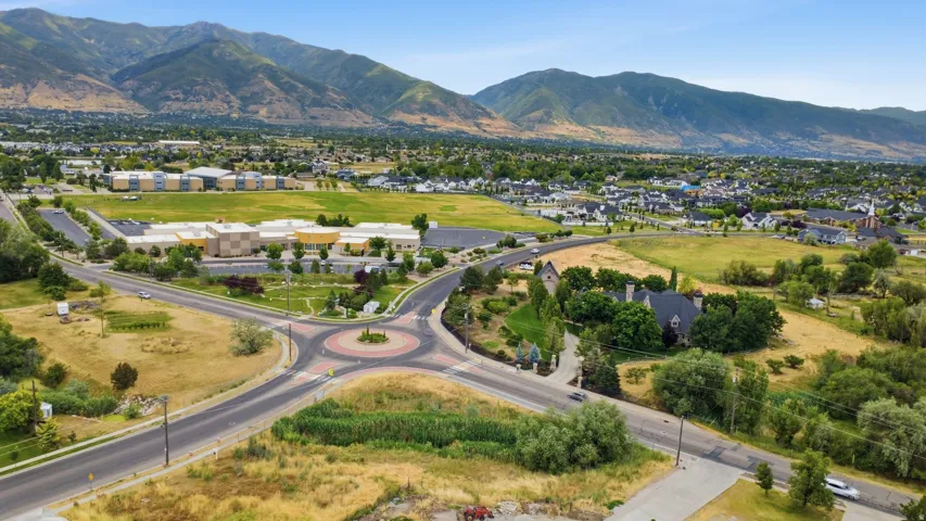 Aerial perspective showcasing a residential area with a prominent roundabout, surrounded by green spaces and distant mountains