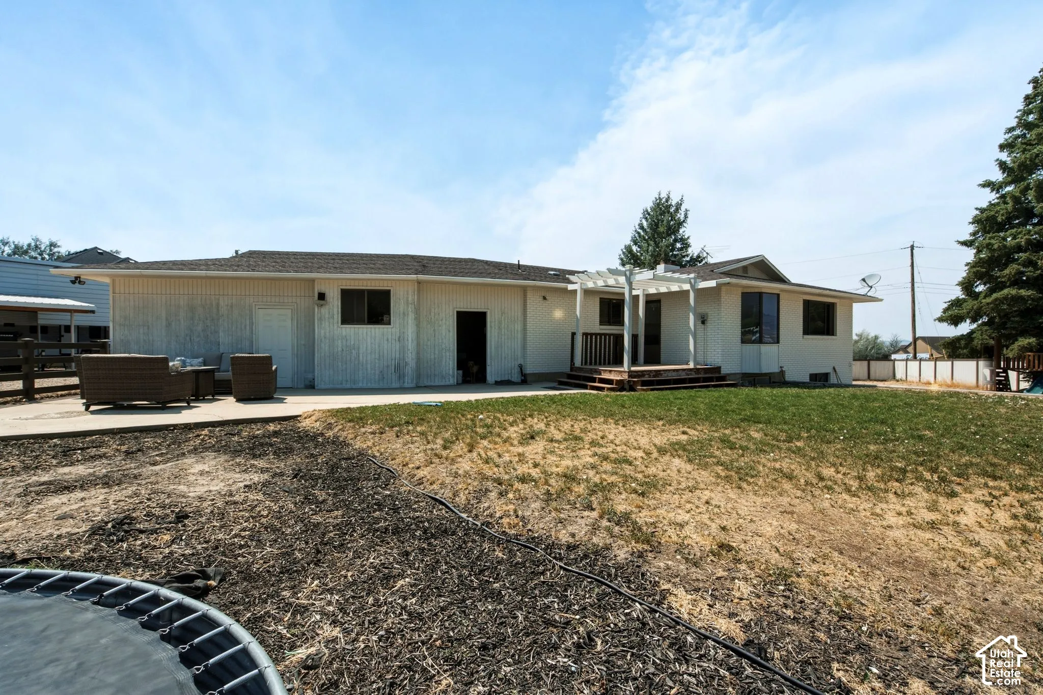 Rear exterior featuring a wood deck with pergola, concrete patio area, and an expansive lawn