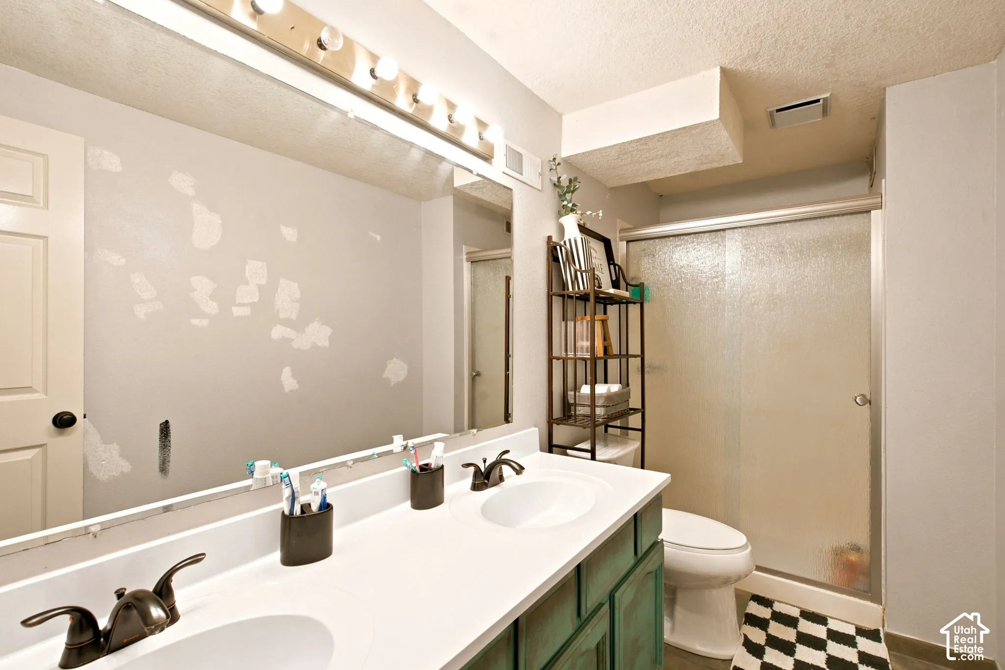 Bathroom featuring a dual vanity with a white countertop and bronze-finish faucets, a shower enclosure with frosted glass sliding doors, and checkered floor tiling