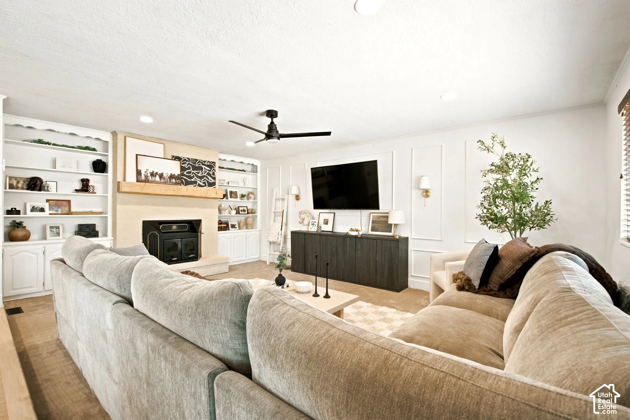 Spacious living area featuring a fireplace with a wood mantle, built-in shelving, sconce lighting, and ceiling fan
