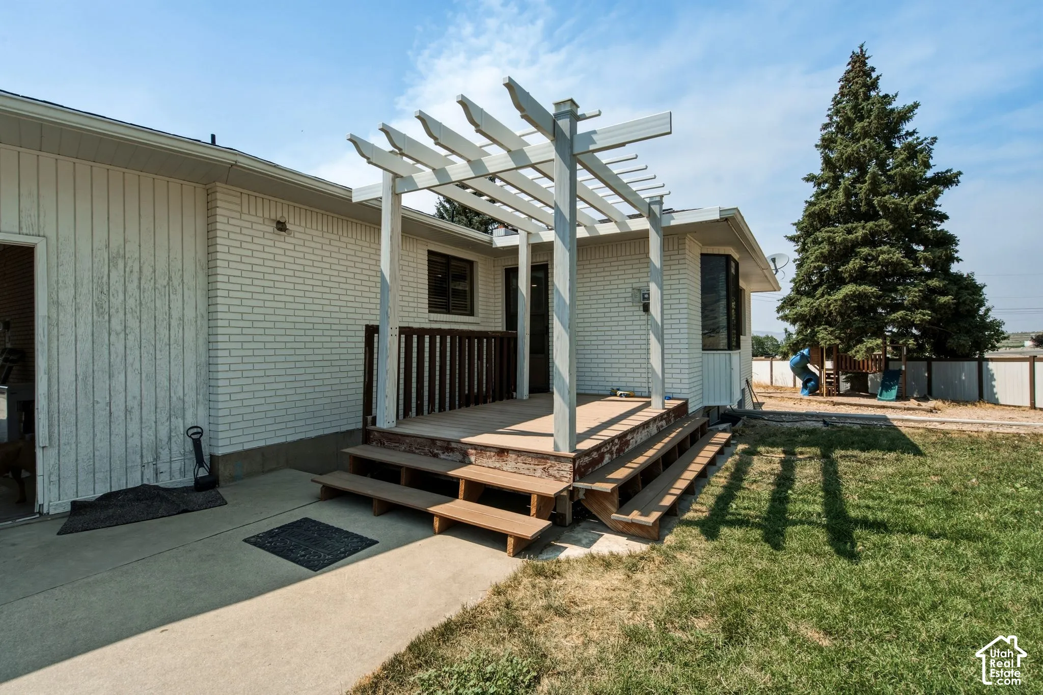 Exterior featuring white brick siding and a wood deck with an attached pergola