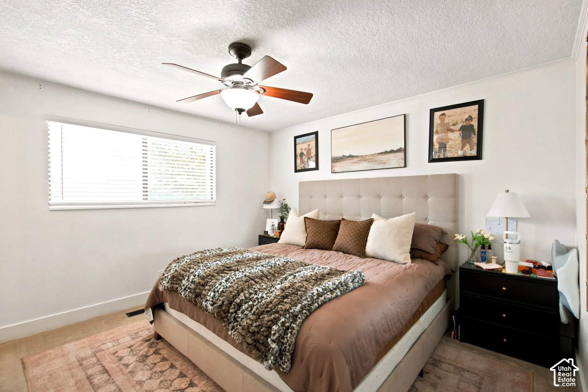 Bedroom featuring a ceiling fan with integrated lighting, a rectangular window with horizontal blinds, and a neutral upholstered headboard