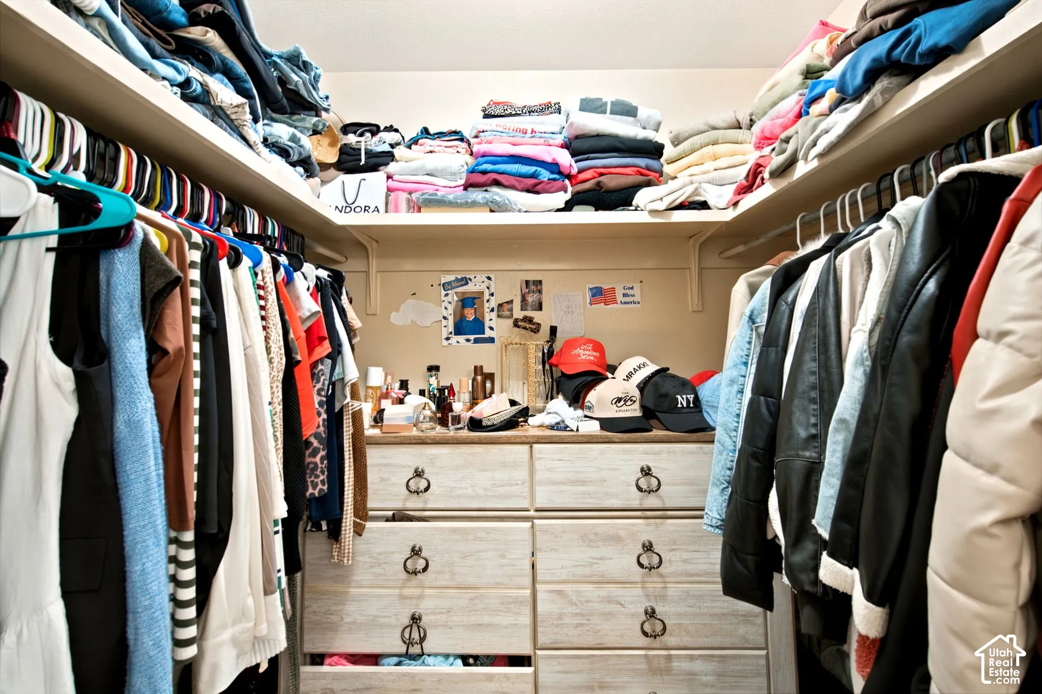 Walk-in closet featuring extensive built-in shelving, multiple hanging rods, and a central built-in dresser with multiple drawers