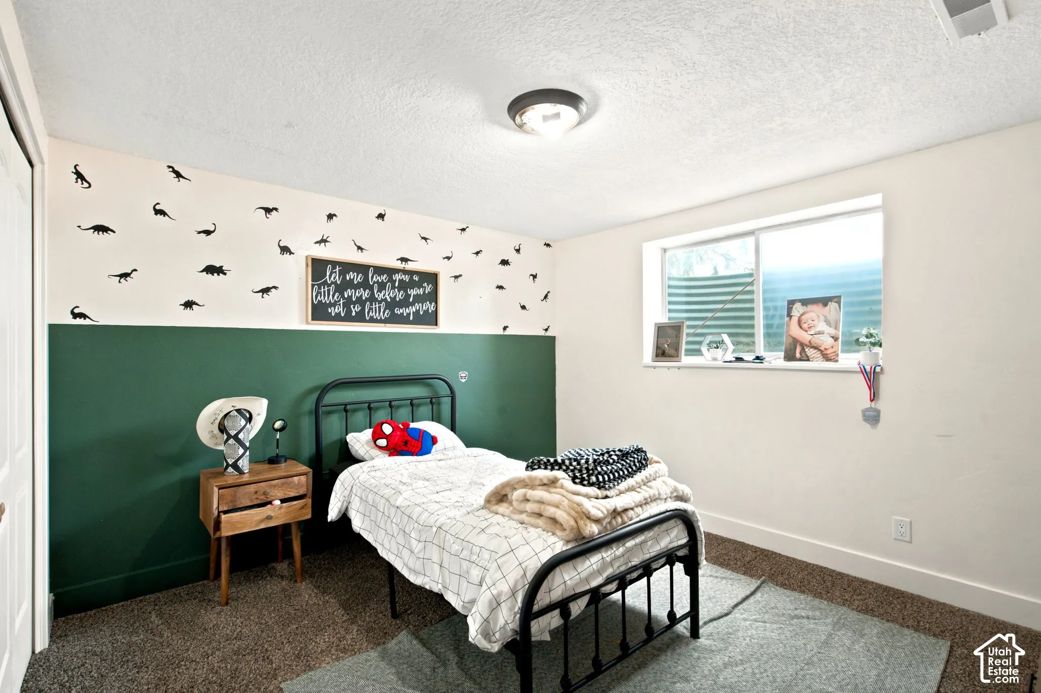 Room featuring two-tone walls with a dark green lower section, textured carpet flooring, a single window with a white frame, a built-in closet with white bifold doors, and a ceiling-mounted light fixture