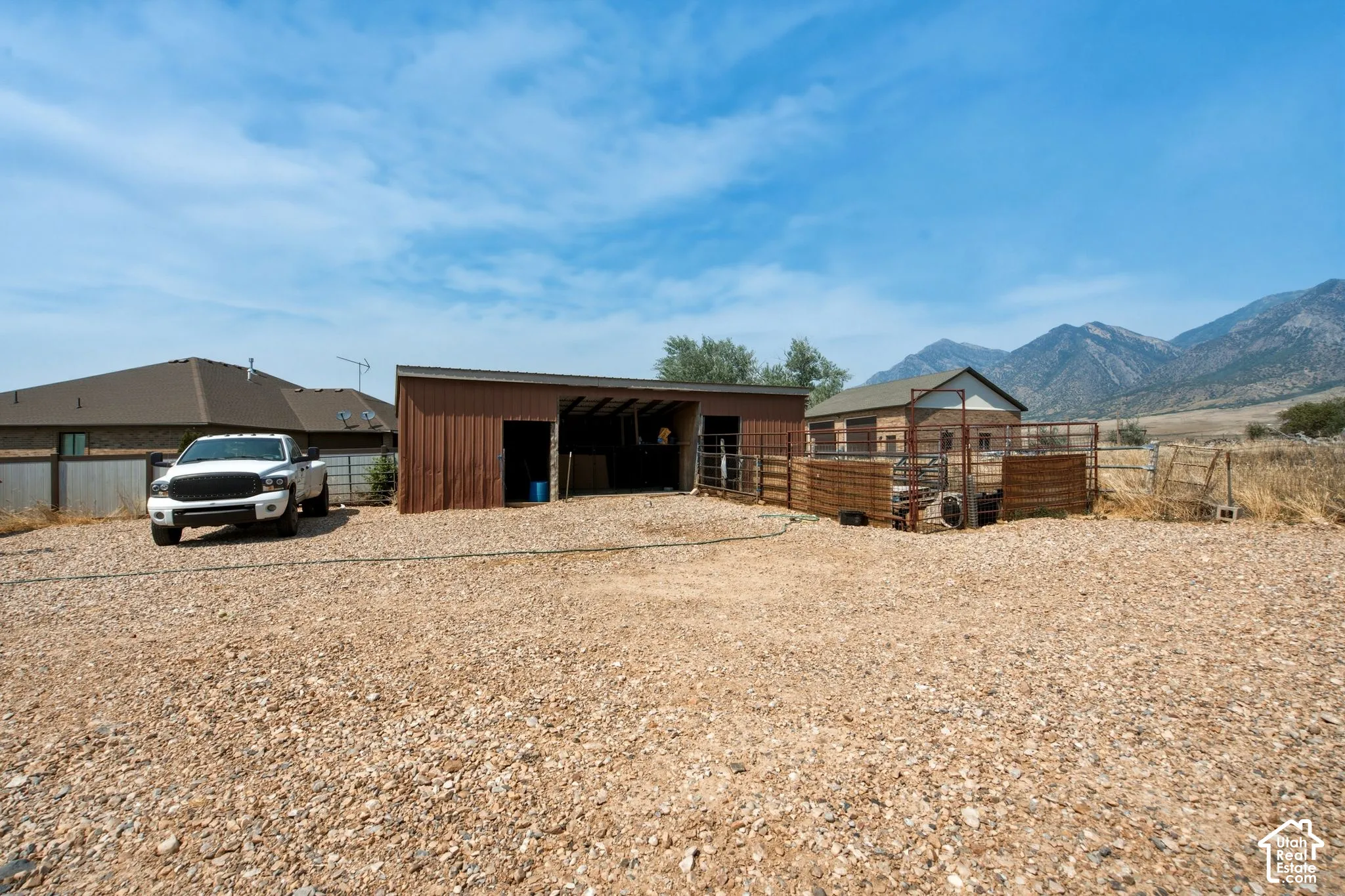 Expansive gravel lot featuring a brown metal shelter and an additional barn structure with exterior fencing