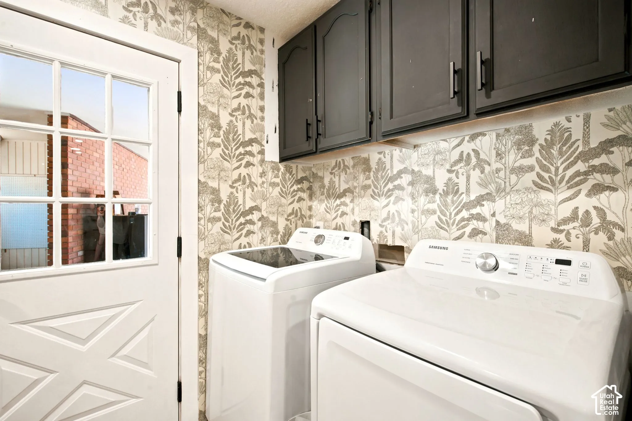 Utility area featuring overhead dark cabinetry, botanical-patterned wallpaper, and a white paneled door with glass inserts