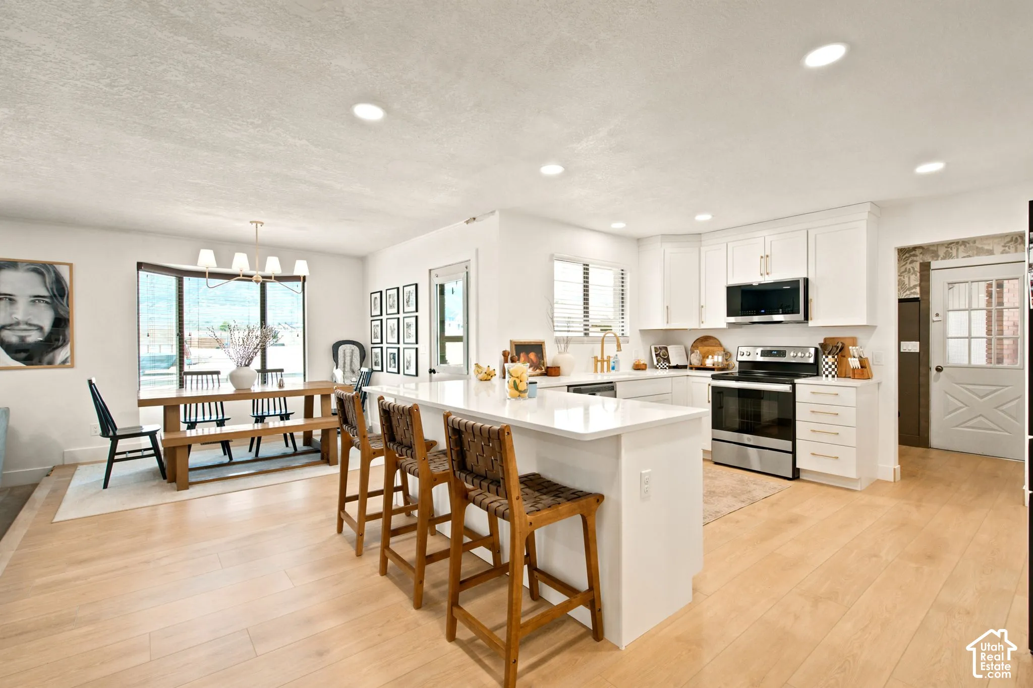 Open-concept kitchen and dining area featuring a spacious island with bar seating, light wood-finish flooring, white cabinetry, stainless steel appliances, and recessed lighting