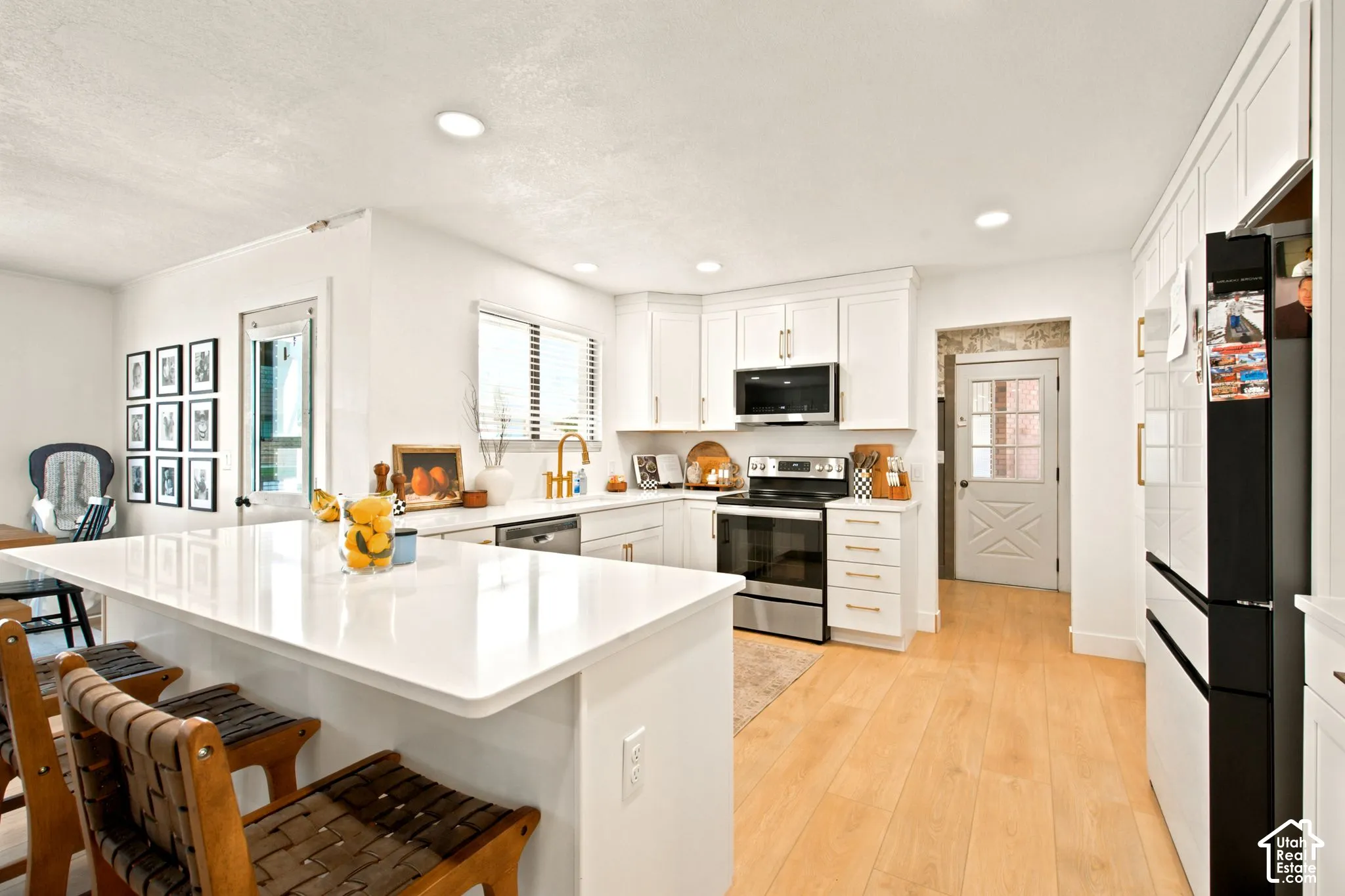 Bright kitchen featuring a white quartz-surfaced island, stainless steel appliances, light wood-finish flooring, white cabinetry, and recessed lighting
