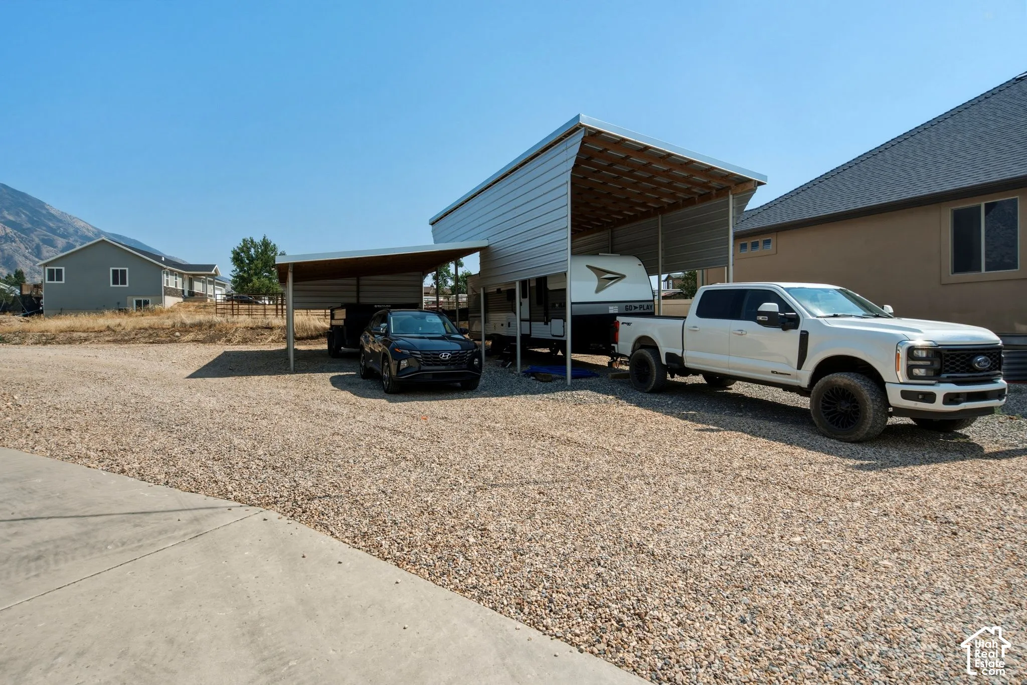 Gravel parking area featuring a large metal carport structure, a smaller metal carport structure, and a concrete pad portion