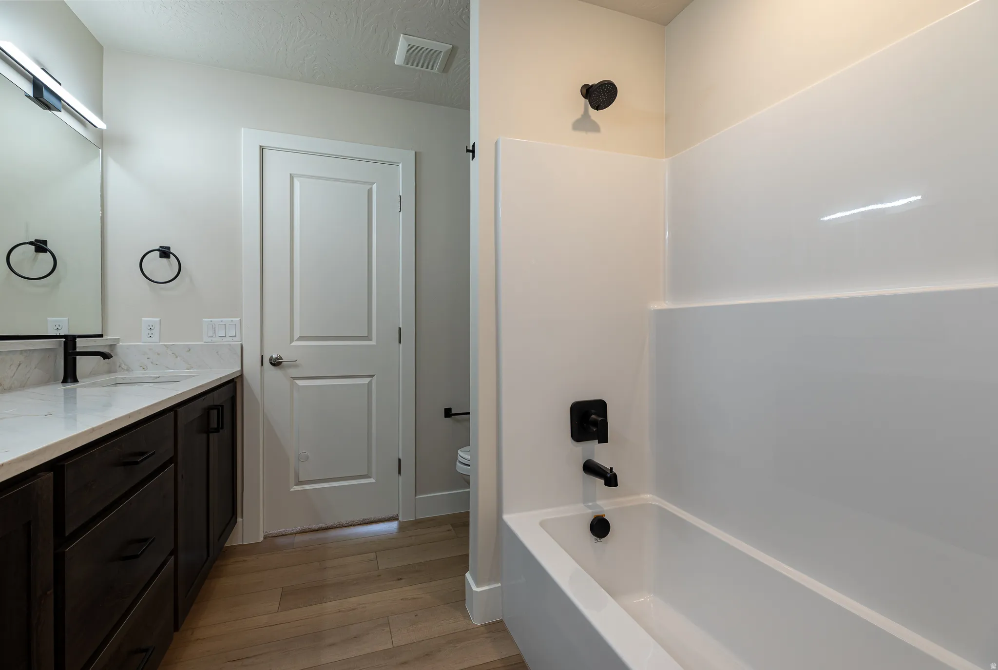 Bathroom featuring a dark wood-finish vanity with a light countertop, integrated sink, and black fixtures