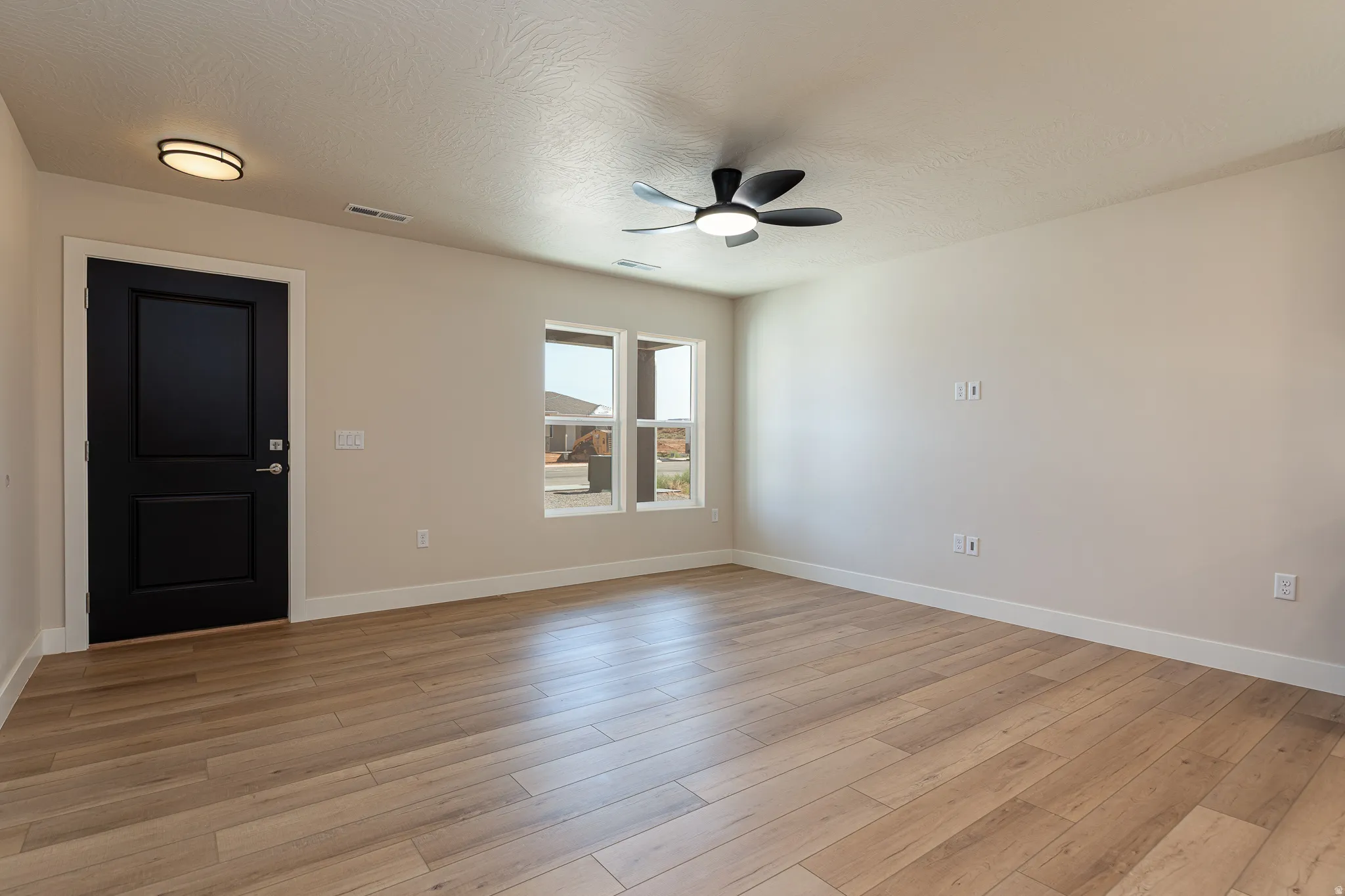 Spacious room featuring wood-finish flooring, light-toned walls, and a modern ceiling fan