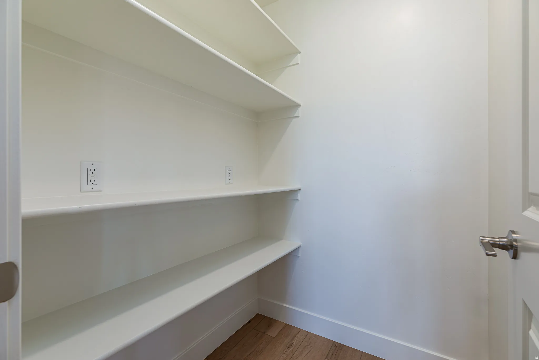 Walk-in pantry featuring white shelving, light wood-finish flooring, and white baseboards