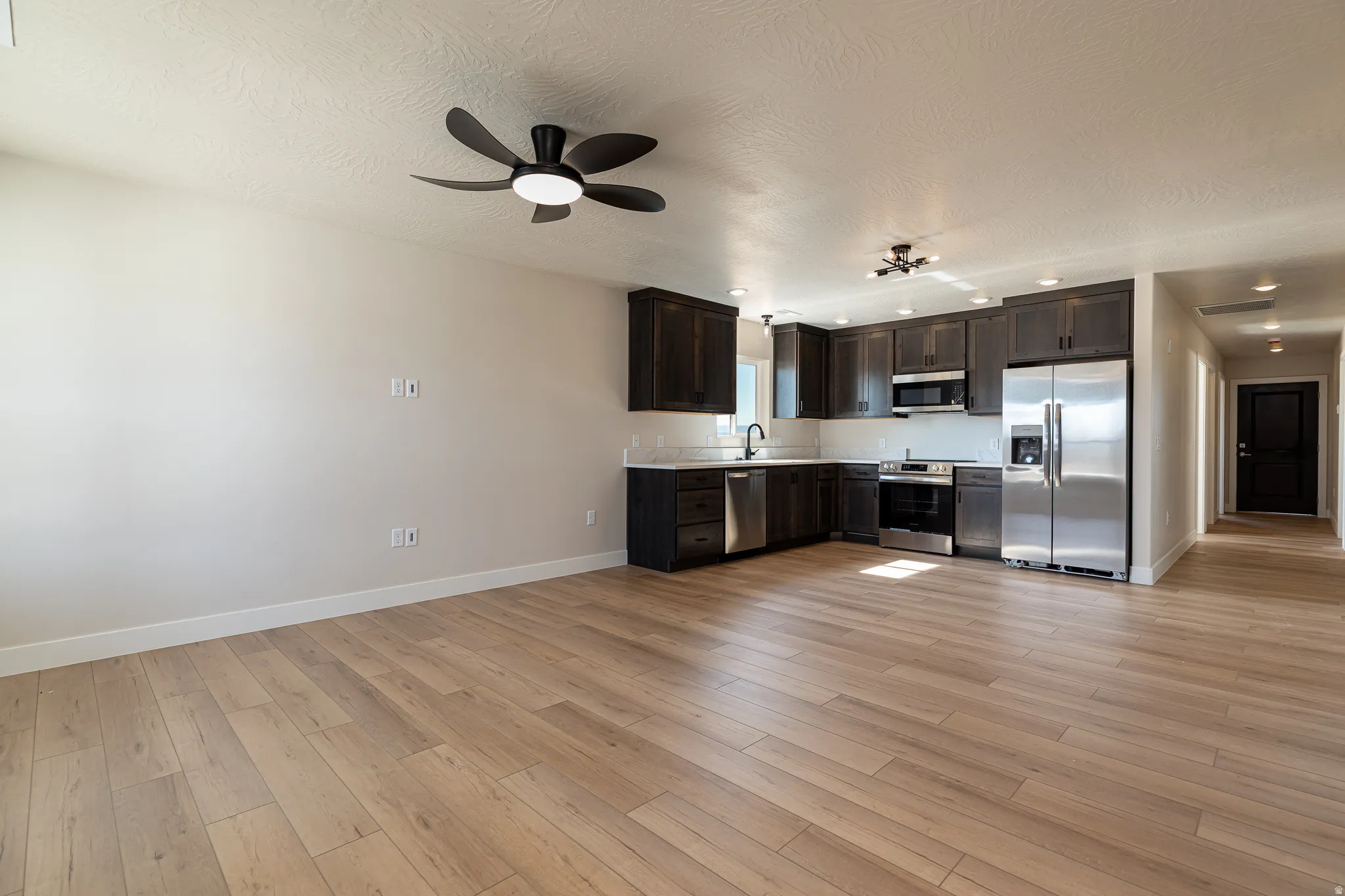 Open-concept living space featuring wood-finish flooring, a modern ceiling fan, dark wood cabinetry, stainless steel appliances, and recessed lighting