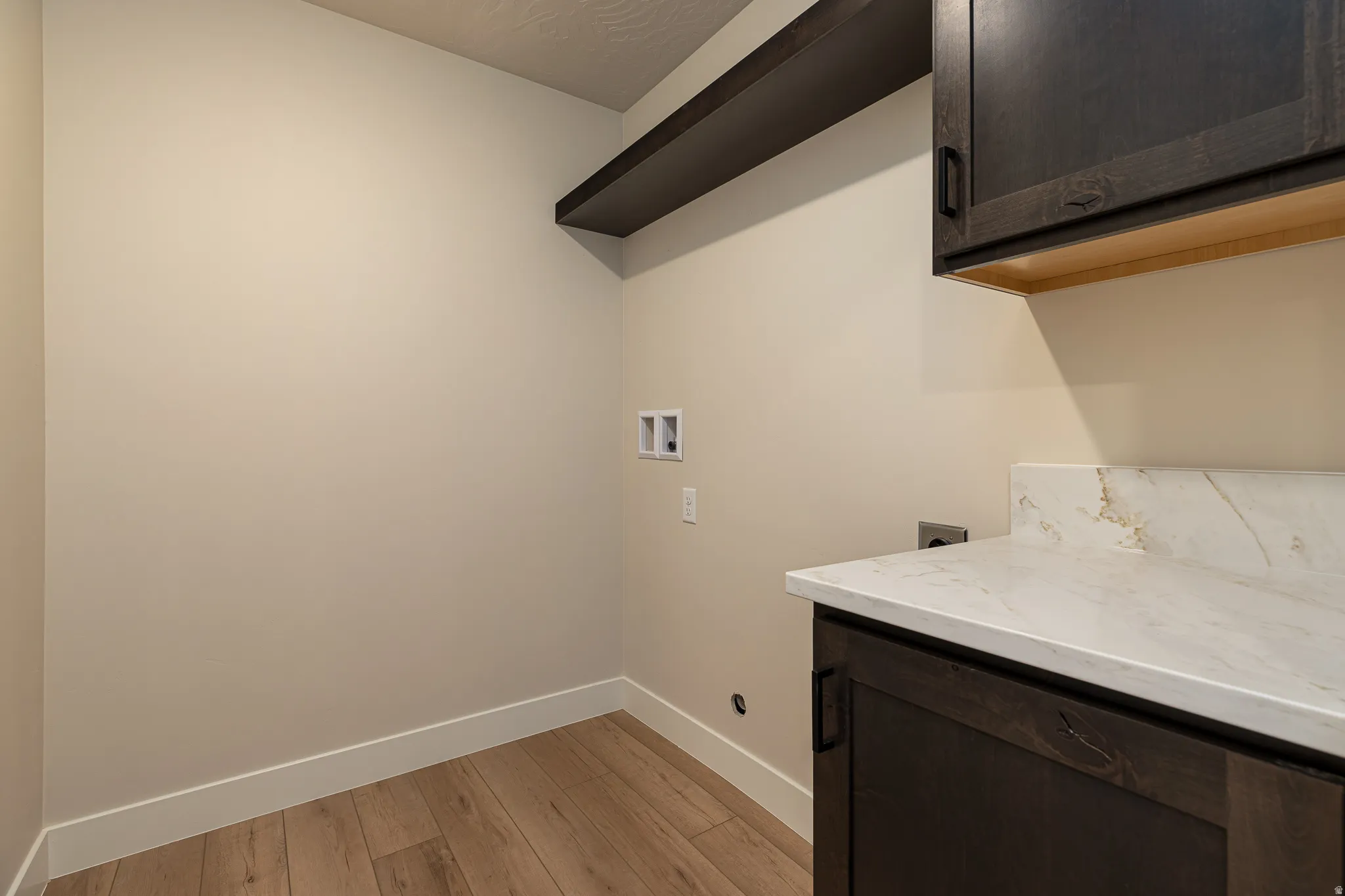Utility room featuring wood-finish flooring, light-toned walls, and a built-in dark wood cabinet with a white countertop