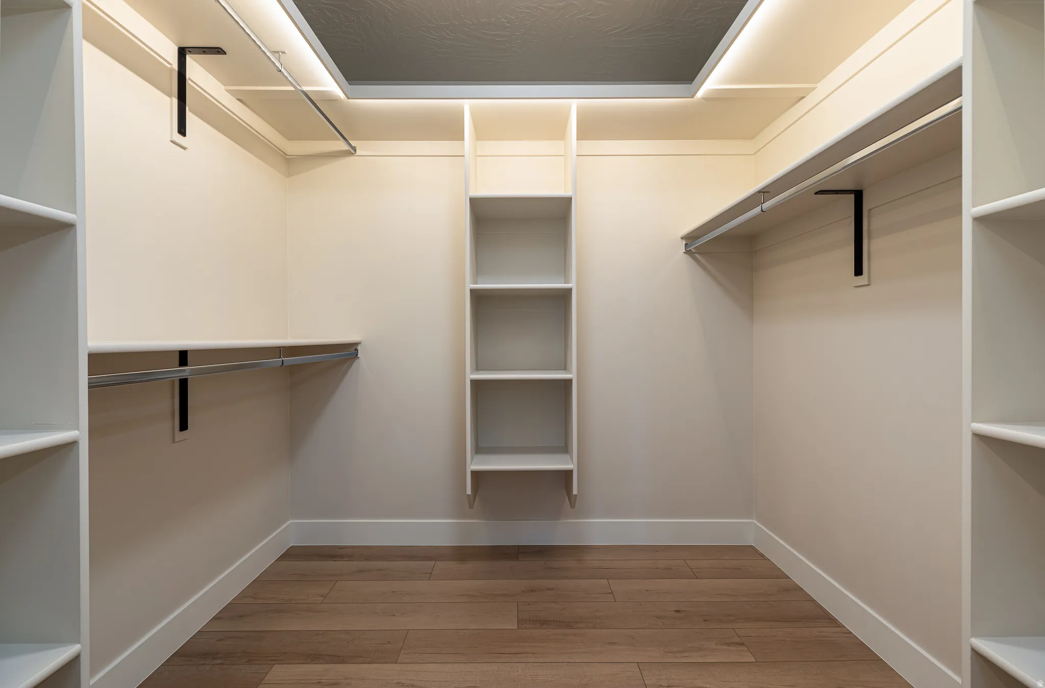 Spacious walk-in closet featuring wood-finish flooring, extensive built-in shelving, multiple clothing rods, and recessed ceiling lighting