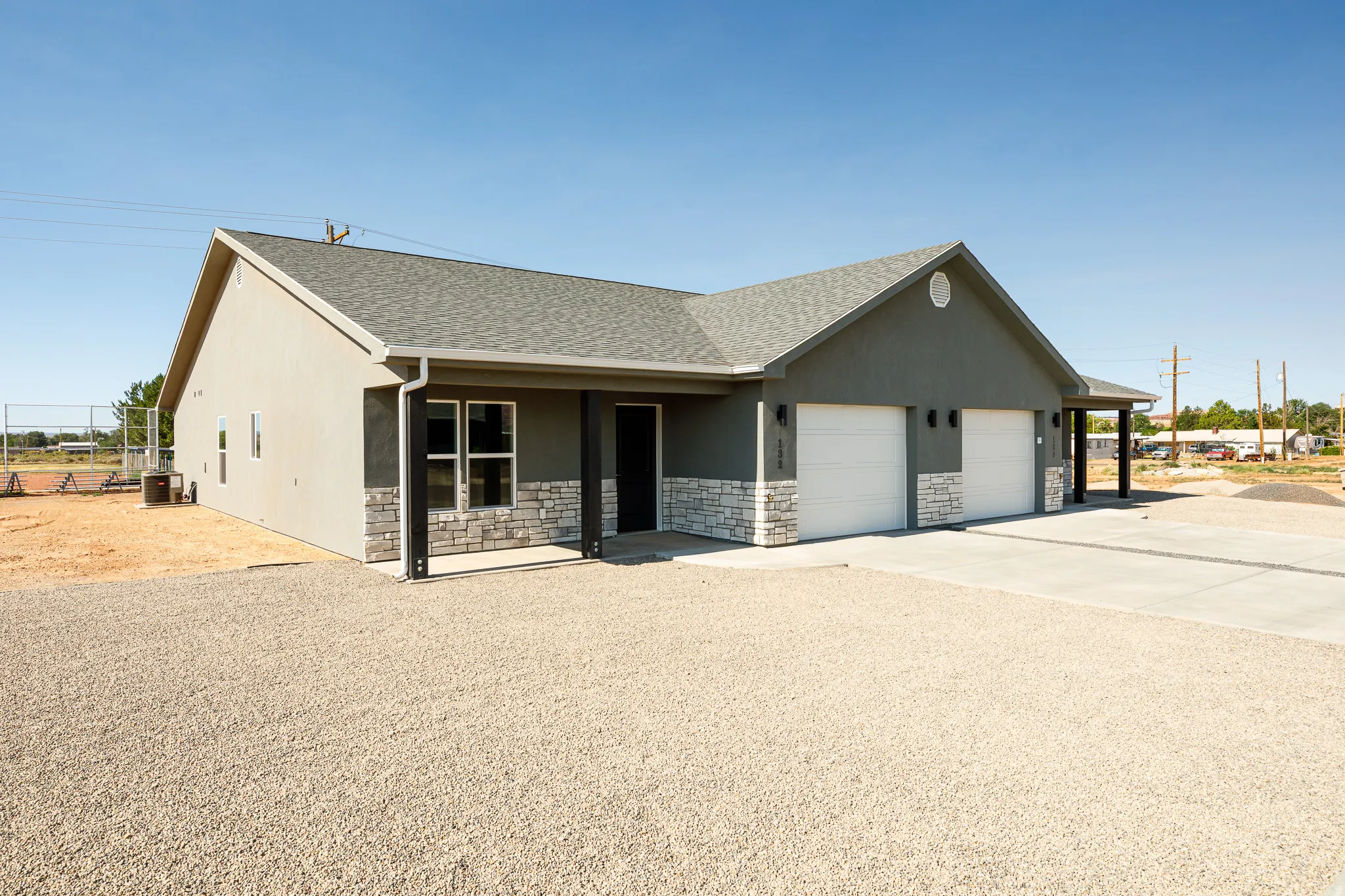 Contemporary exterior featuring gray stucco, stone veneer accents, an asphalt shingle roof, a covered entry, and a two-car garage with concrete driveway