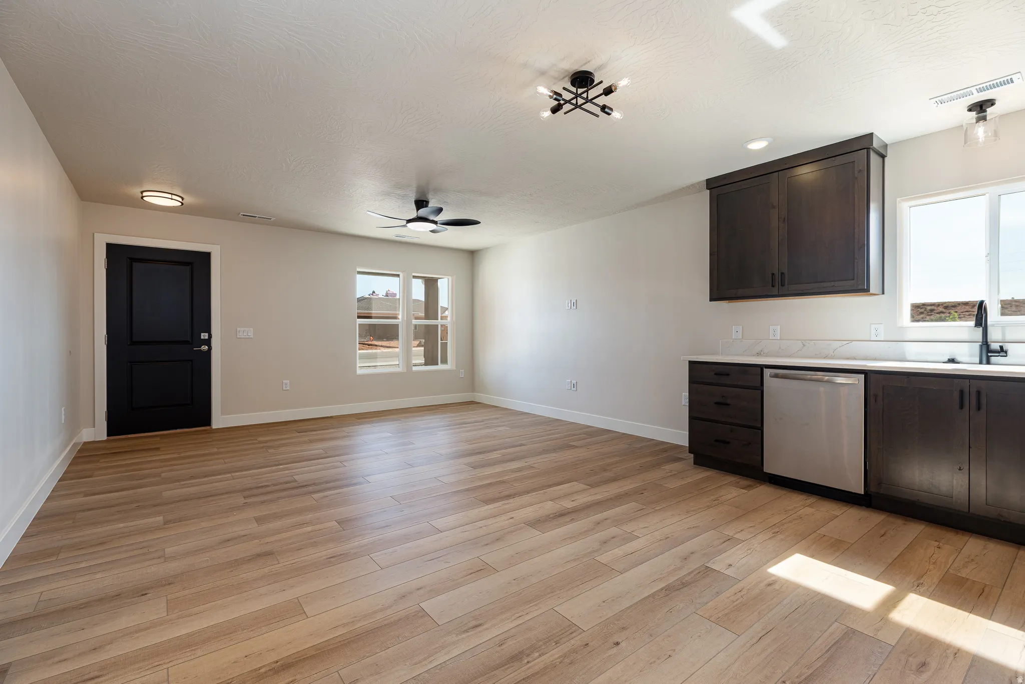 Open-concept living area featuring wood-finish flooring, dark wood cabinetry, a stainless steel dishwasher, and a ceiling fan
