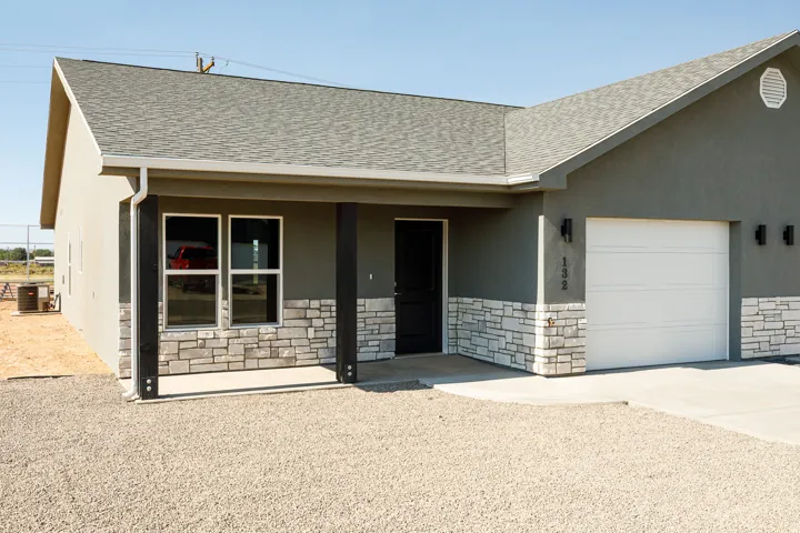 Stucco exterior with stone veneer accents, covered entry, attached garage, and black exterior lighting fixtures