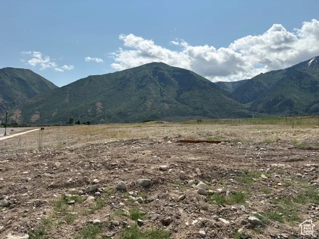Expansive undeveloped land featuring a mountain backdrop, partial fencing, and a concrete pathway