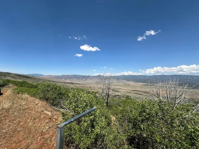 Expansive natural landscape under a clear blue sky, featuring distant mountains and broad plains