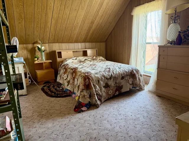 Attic bedroom featuring angled wood-paneled walls and a window with sheer curtains