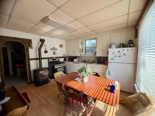 Kitchen featuring wood-finish flooring, a freestanding gas range, white cabinetry, and a wood-burning stove