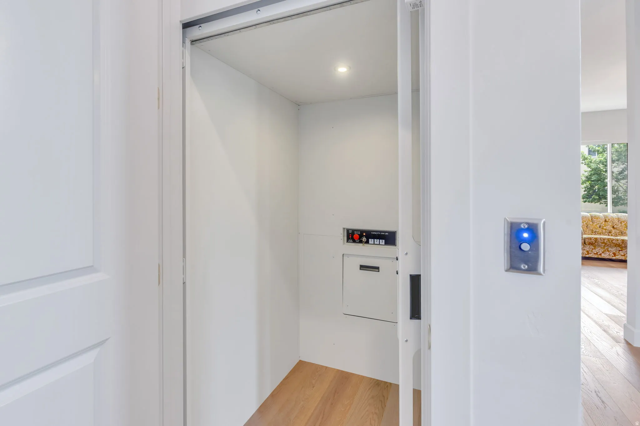 Interior residential elevator featuring light wood-finish flooring, recessed lighting, and a control panel