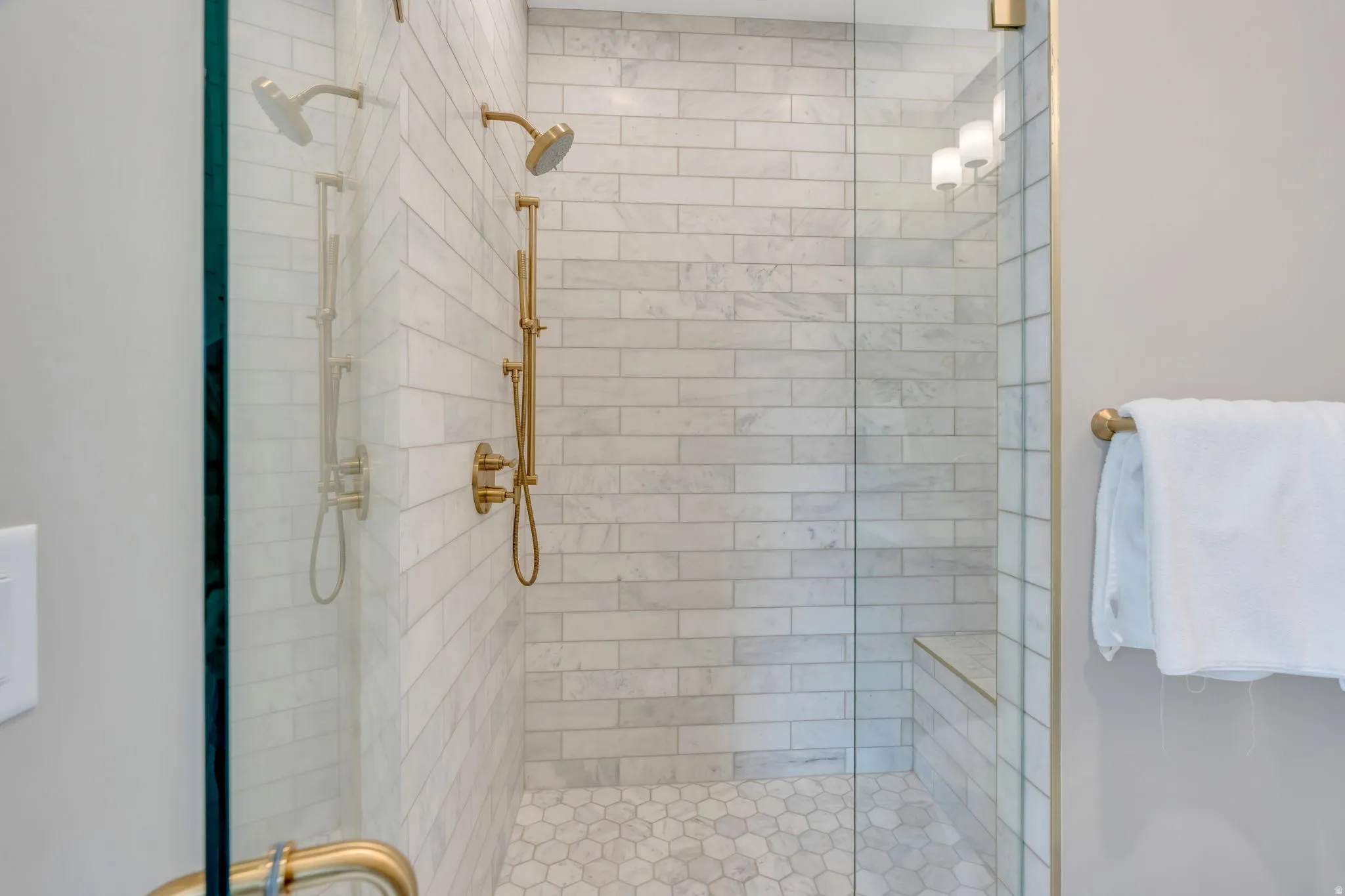Glass-enclosed shower featuring white subway tile, a built-in bench, hexagonal floor tiles, a dual shower head system, and brass fixtures