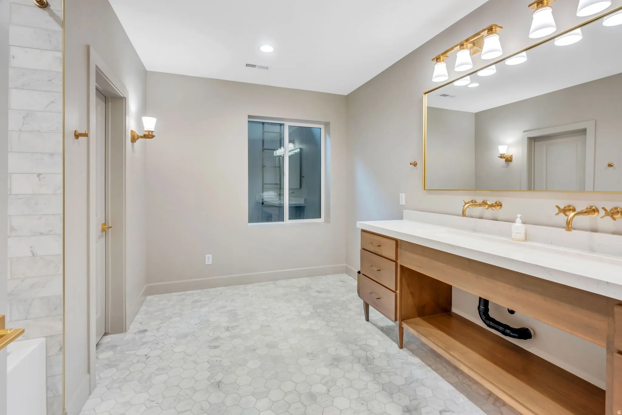Spacious bathroom featuring a double vanity with a light wood-finish cabinet, white countertop, and gold-finish wall-mounted faucets