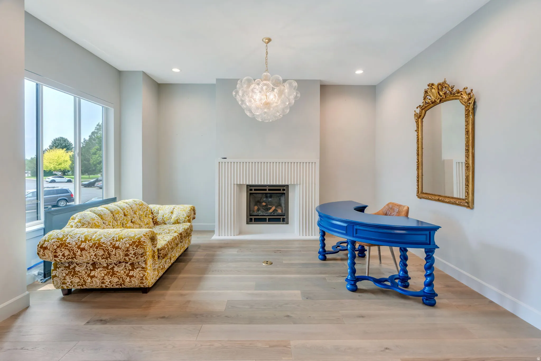Spacious room featuring light wood-finish flooring, a contemporary fireplace with a fluted surround, large windows, recessed lighting, and a bubble chandelier