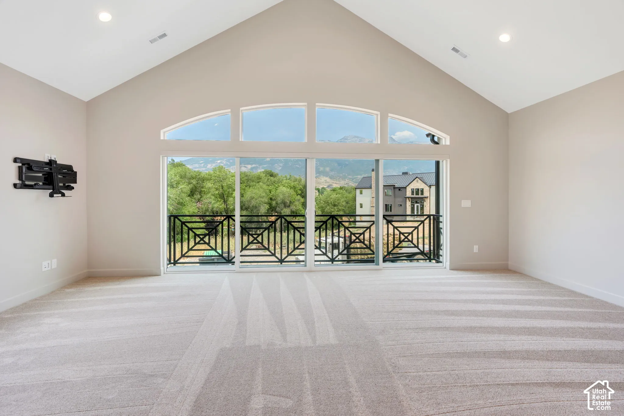 Spacious room featuring vaulted ceilings, a large sliding glass door, arched transom windows, recessed lighting, and a private balcony with decorative iron railings