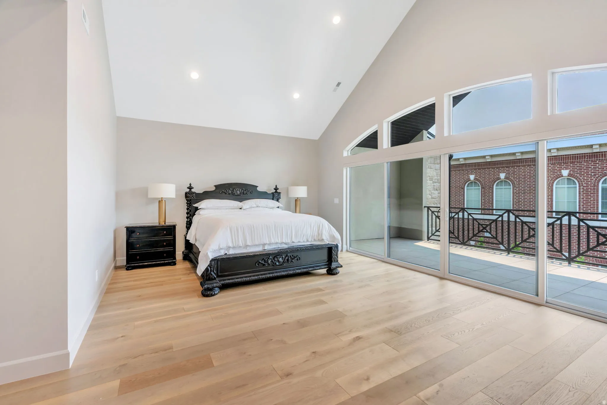 Vaulted ceiling room featuring light wood-finish flooring, recessed lighting, and a full wall of sliding glass doors opening to a balcony with black metal railings