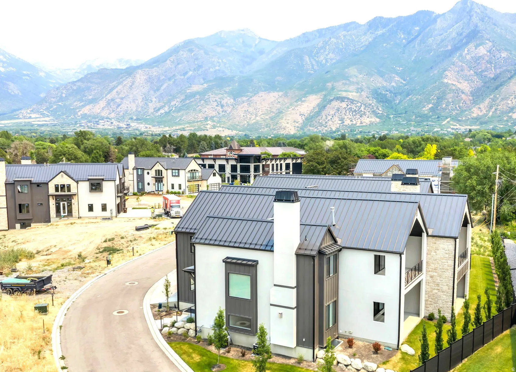 Modern residential structures featuring light-colored siding, dark metal roofs, and stone accents