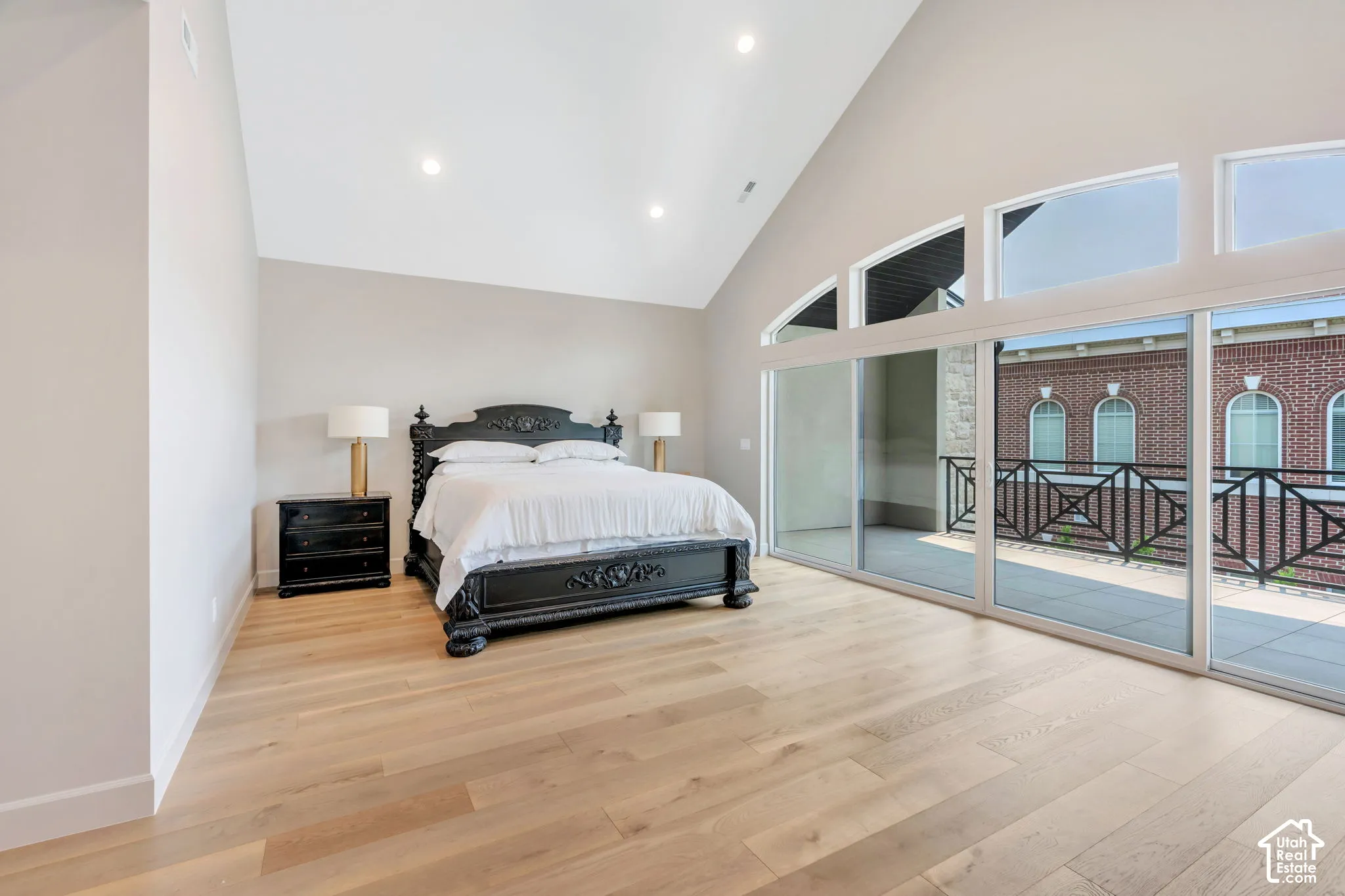 Vaulted ceiling room featuring light wood-finish flooring, recessed lighting, and a full wall of sliding glass doors opening to a balcony with black metal railings