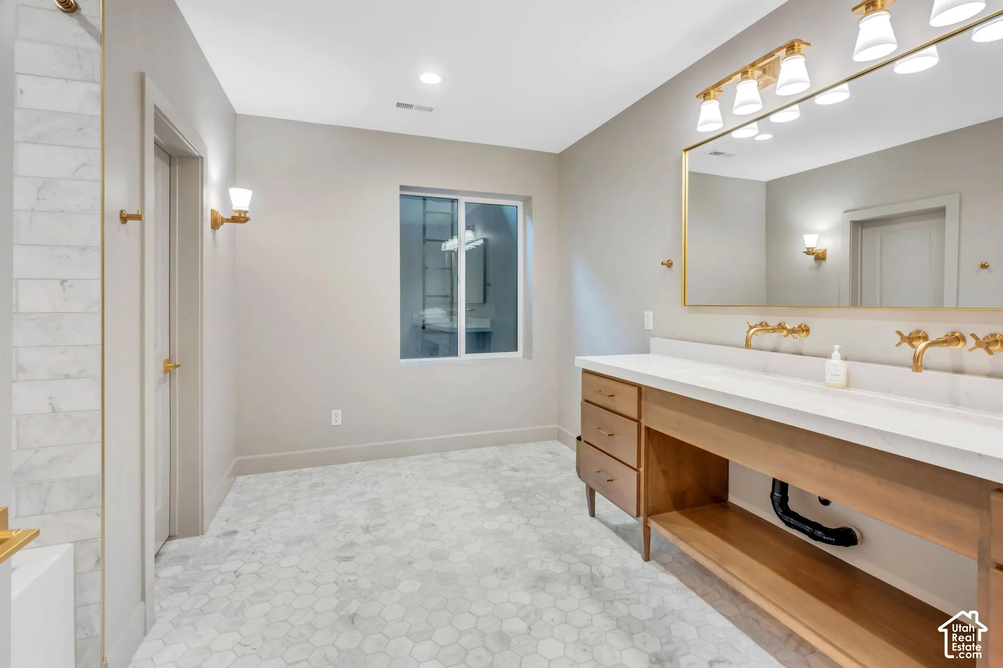 Spacious bathroom featuring a double vanity with a light wood-finish cabinet, white countertop, and gold-finish wall-mounted faucets