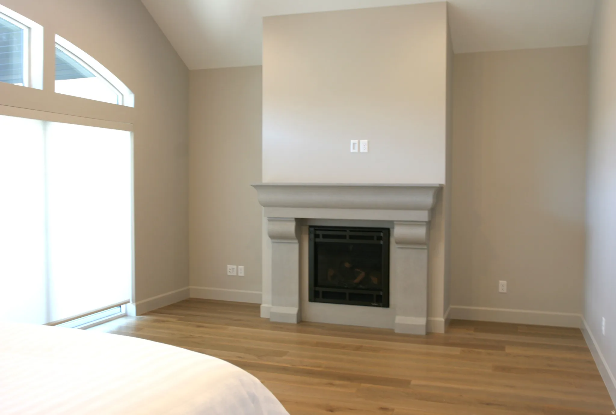 Stone fireplace with mantel, hardwood flooring, vaulted ceiling, and arched transom windows