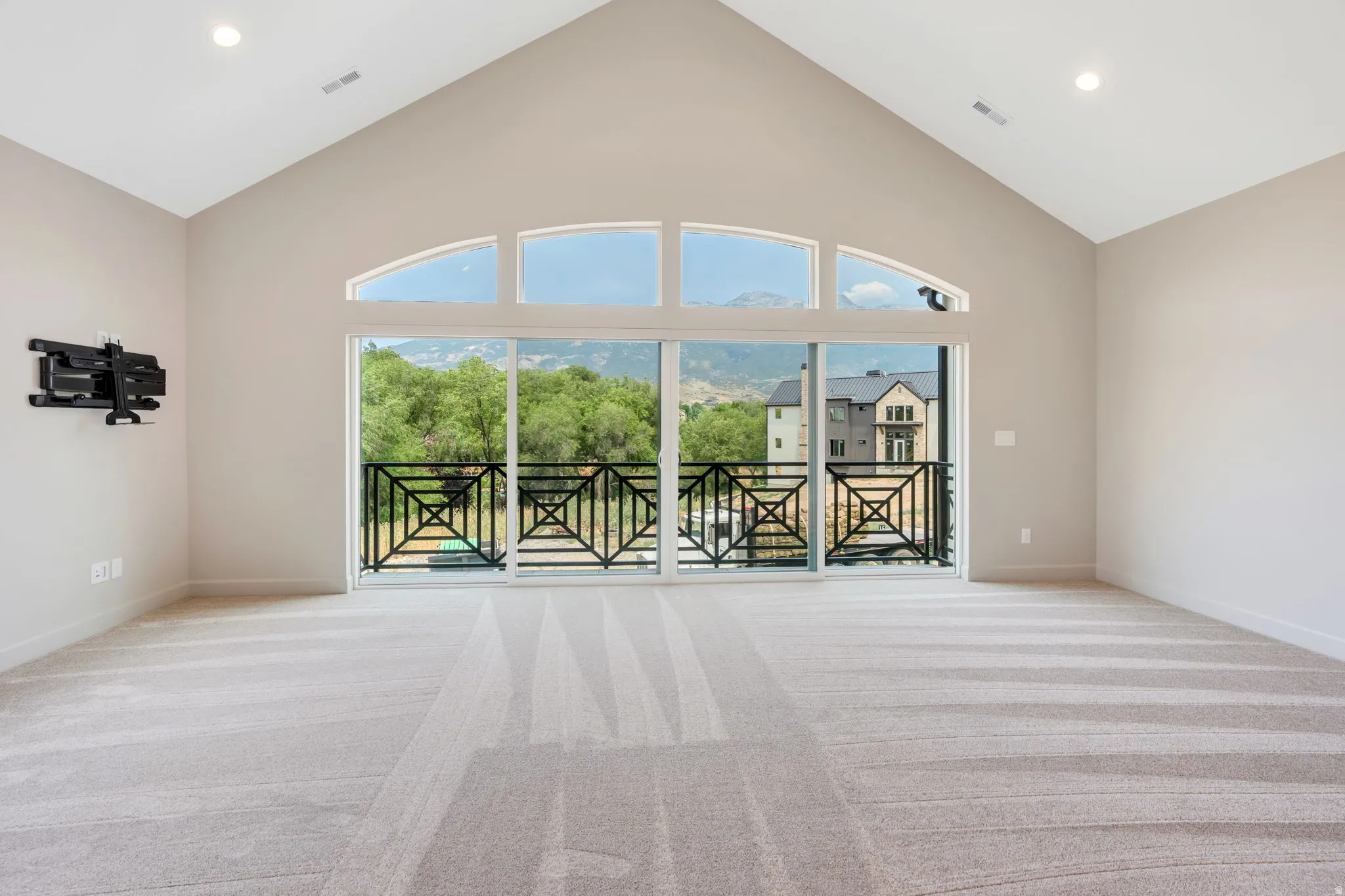 Spacious room featuring vaulted ceilings, a large sliding glass door, arched transom windows, recessed lighting, and a private balcony with decorative iron railings